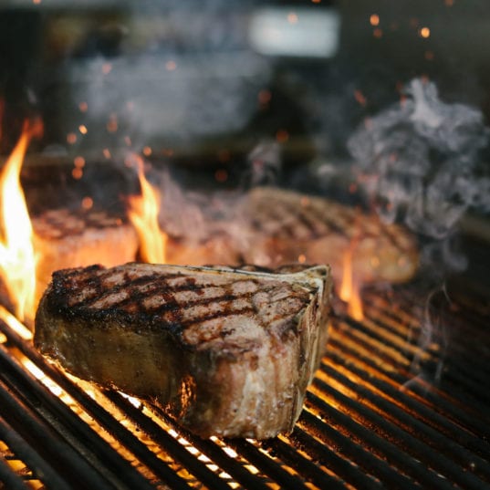 A steak being cooked on a hot grill with flames